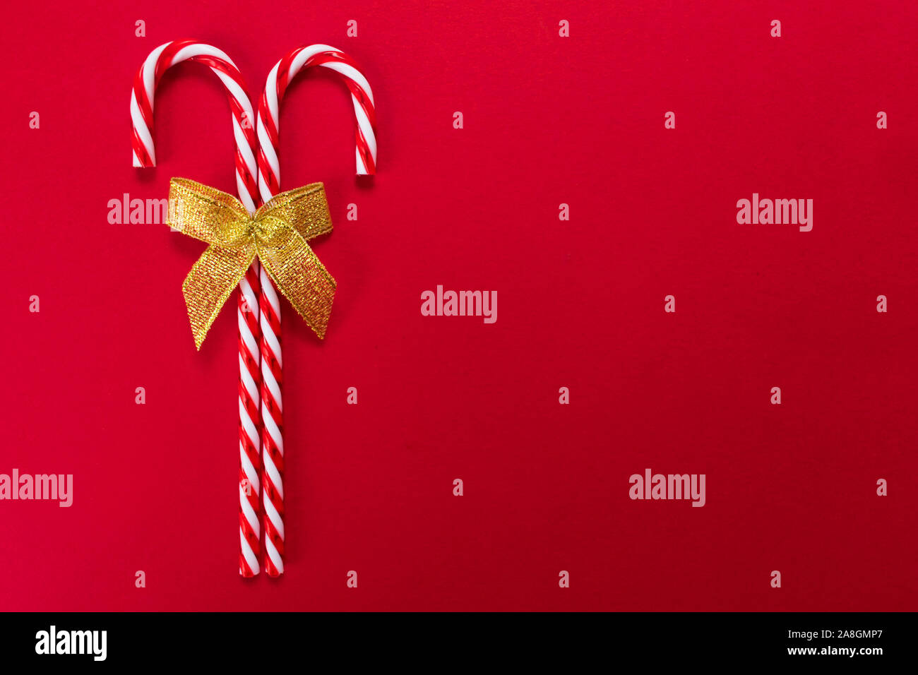 Two christmas candy canes with golden bow on red background. Copy space. Stock Photo