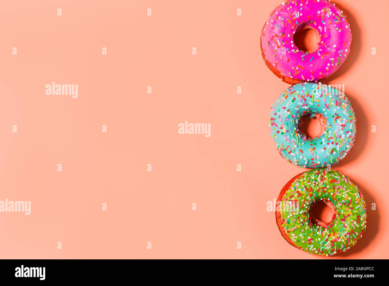 Closeup of three multicolored pink, blue and green glazed sweet donuts on coral background with copy space Stock Photo