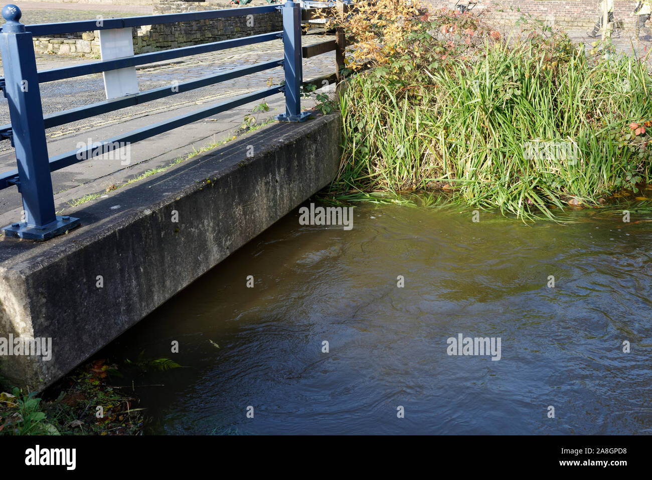 Canal feeder water at high level flowing under concrete footbridge in burrs country park bury lancashire uk Stock Photo