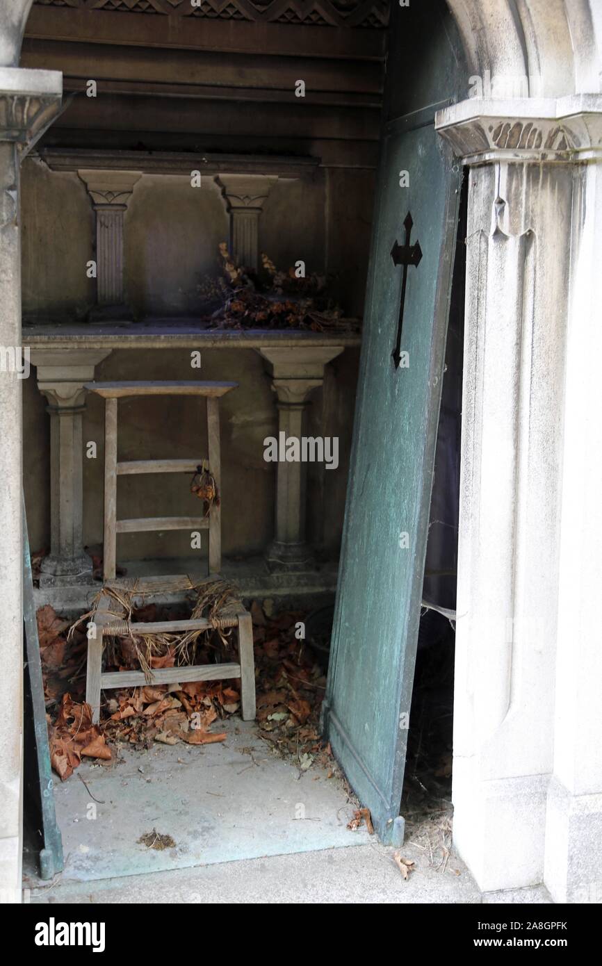 unhinged door and old broken chair on burial loculus of the cemetery Stock Photo
