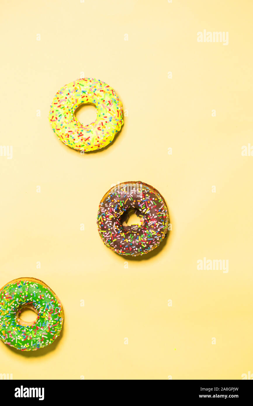 Closeup of three multicolored glazed sweet donuts on a yellow background, top view Stock Photo
