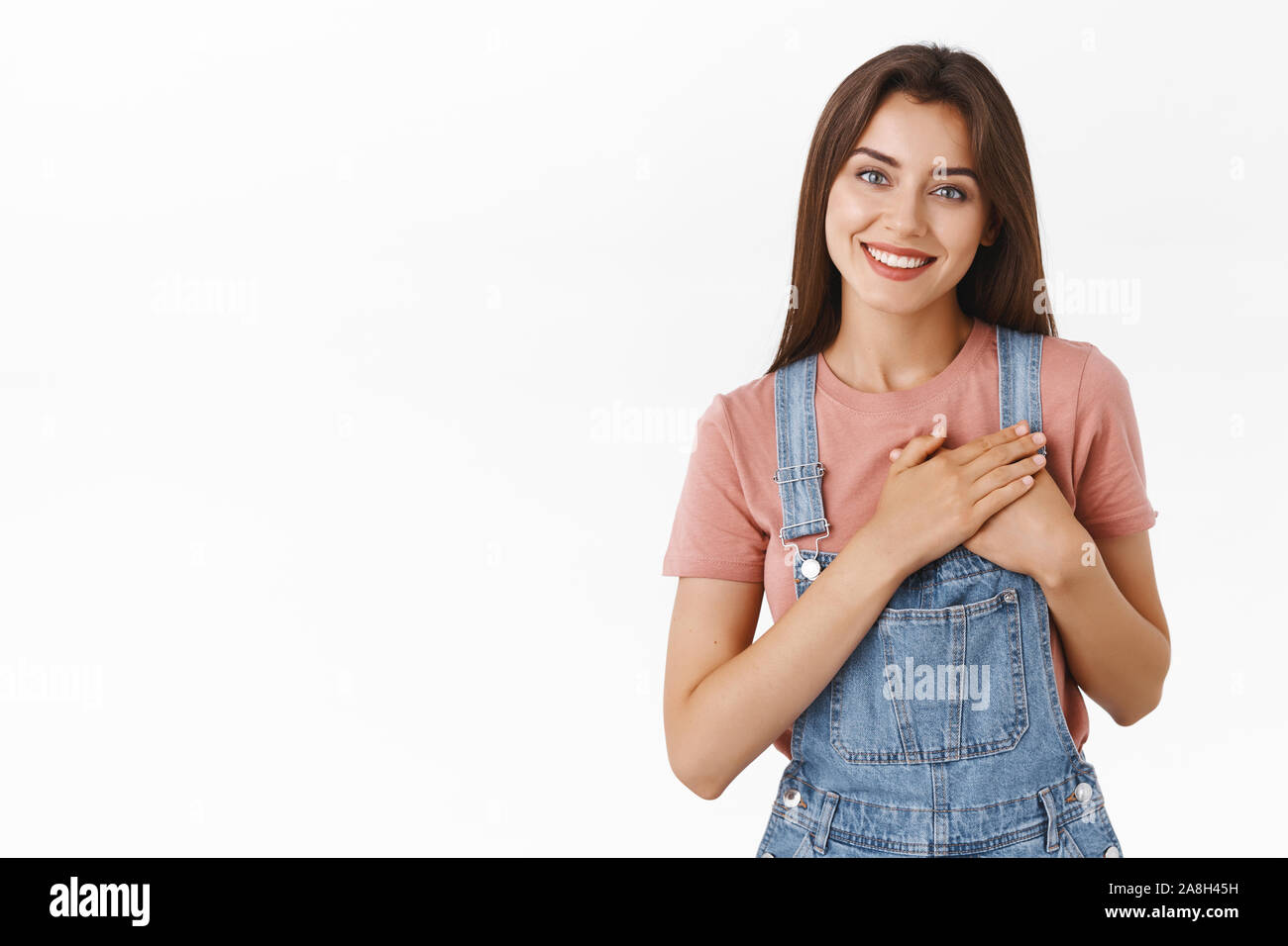 Tender, feminine lovely happy woman in overalls, t-shirt, press hands to heart, tilt head and smiling thanking dearly for help, looking grateful Stock Photo