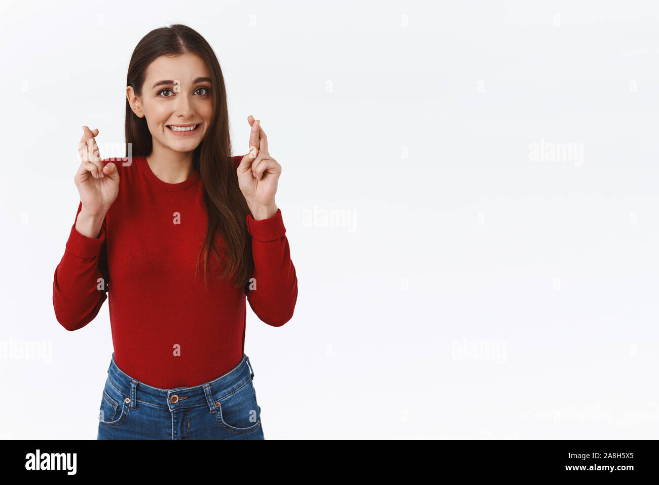 Fingers crossed for everything go well. Slightly nervous cute caucasian girl in red sweater, praying for dream come true, looking excited and worried Stock Photo