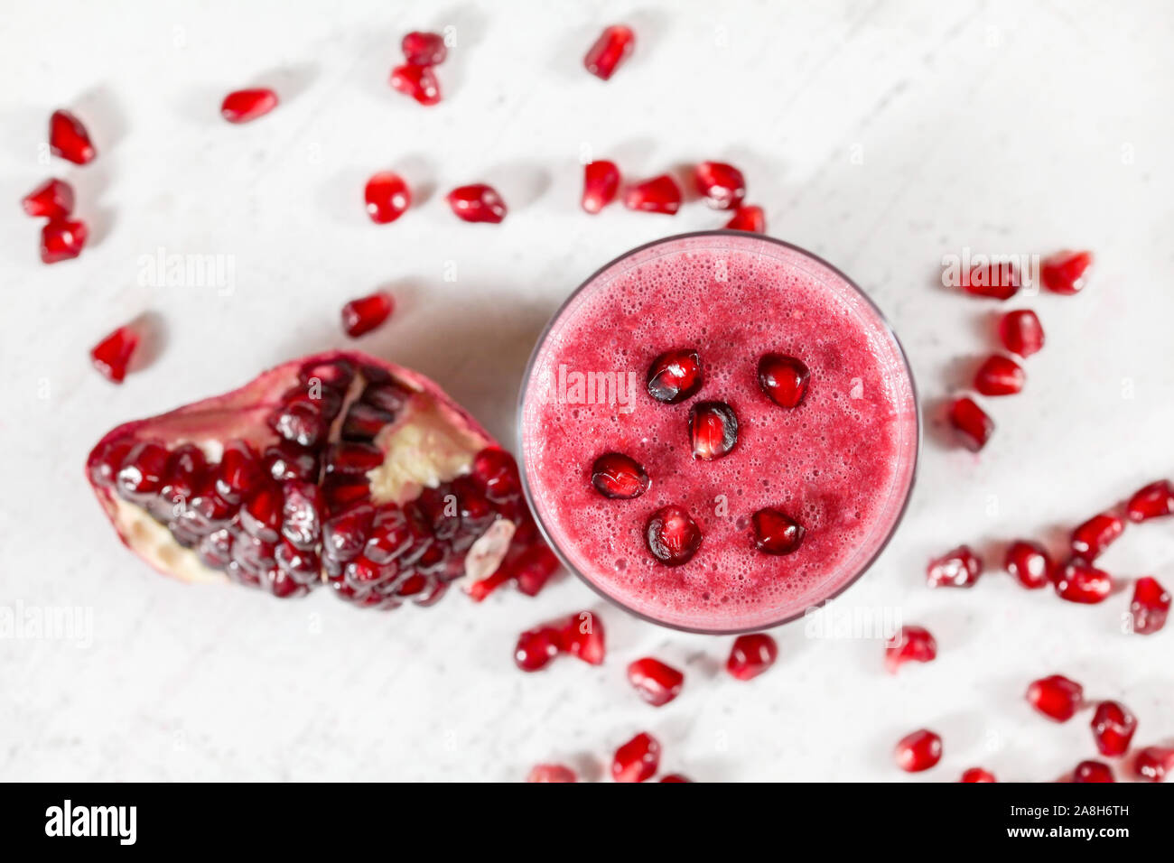 Overhead shot - glass with pomegranate smoothie, fruit berries scattered over white desk around Stock Photo