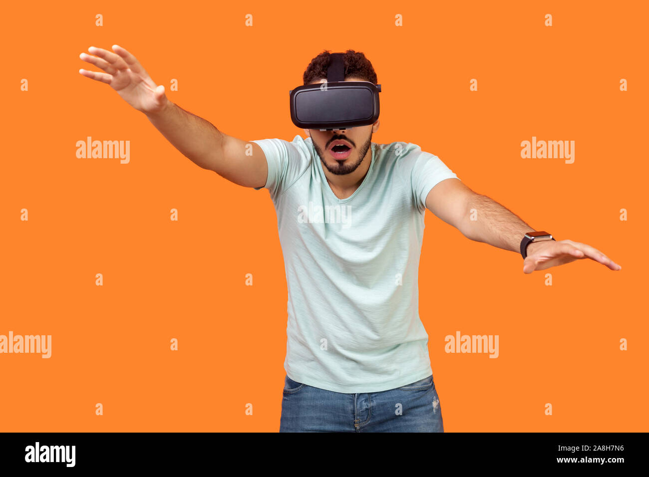 Portrait of frightened gamer, brunette man in t-shirt wearing vr glasses, stretching hands forward, trying to grab something while playing virtual rea Stock Photo