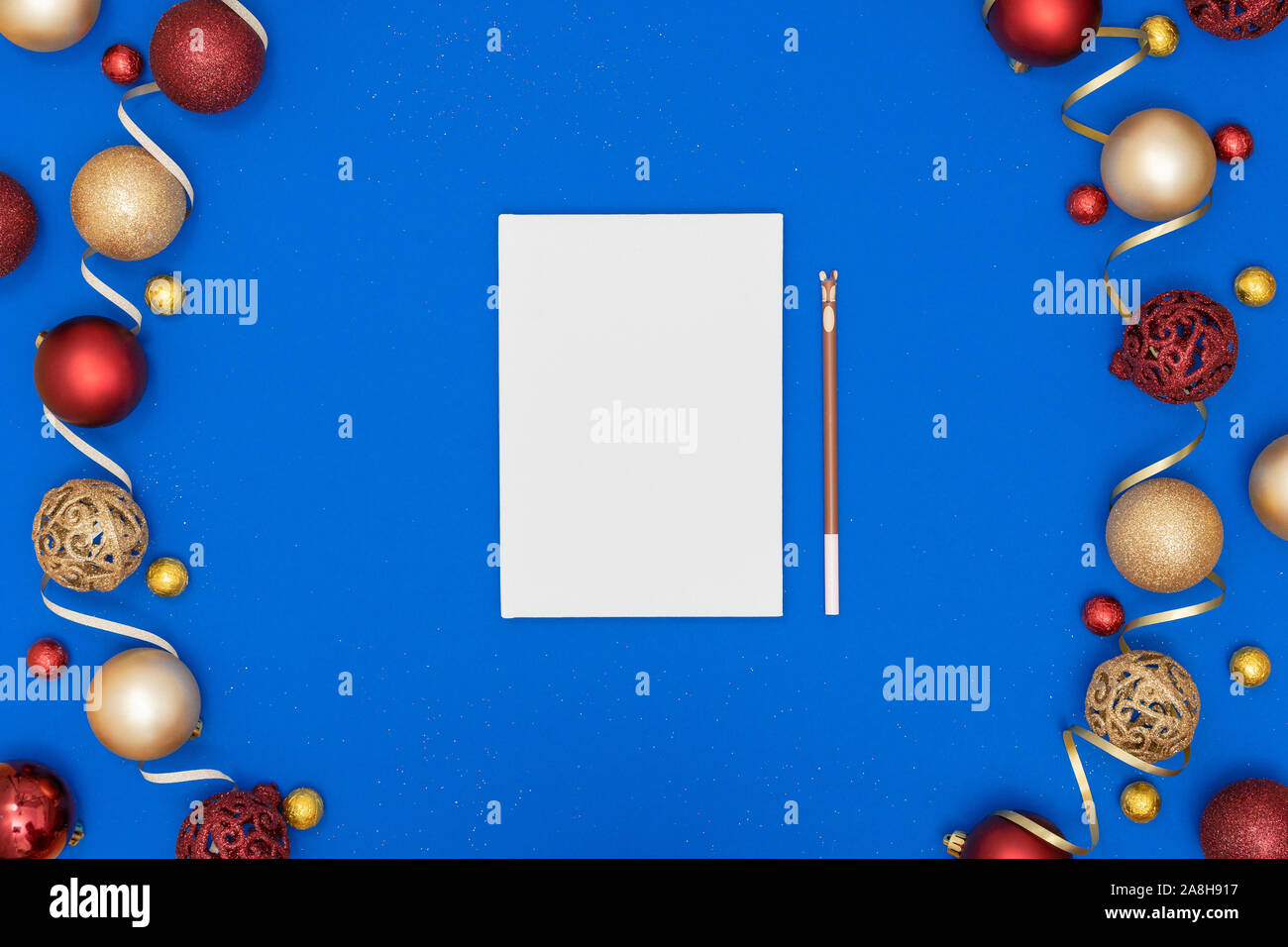 New Year and Christmas decorations and blank white sheet of paper and pencil on blue paper background. Wish list or goals concept. Top view, flat lay, copy space. Stock Photo