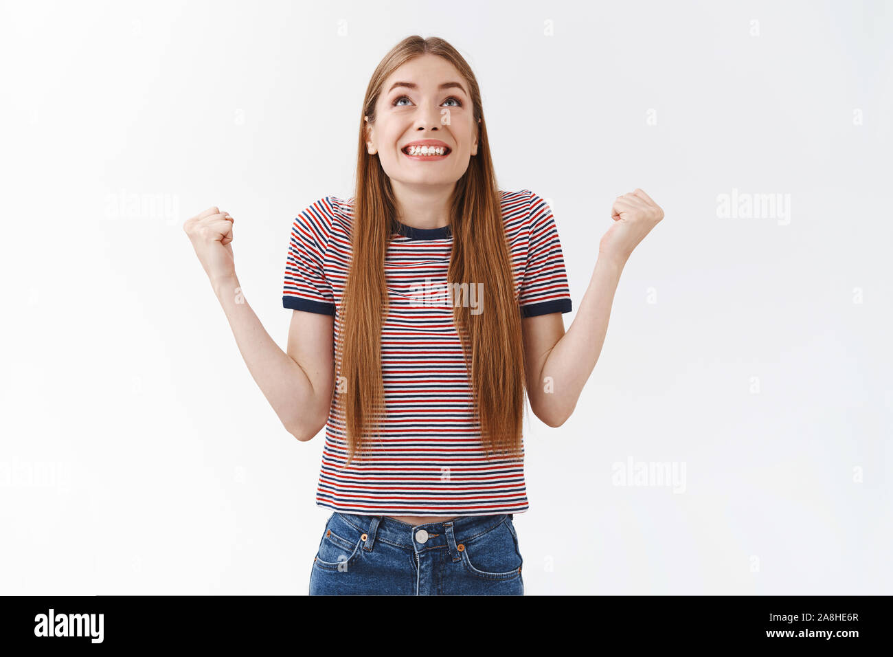 Relieved, happy good-looking woman in striped t-shirt thank god and fist pump cheerfully, look up sky smiling gladly, triumphing from awesome news Stock Photo