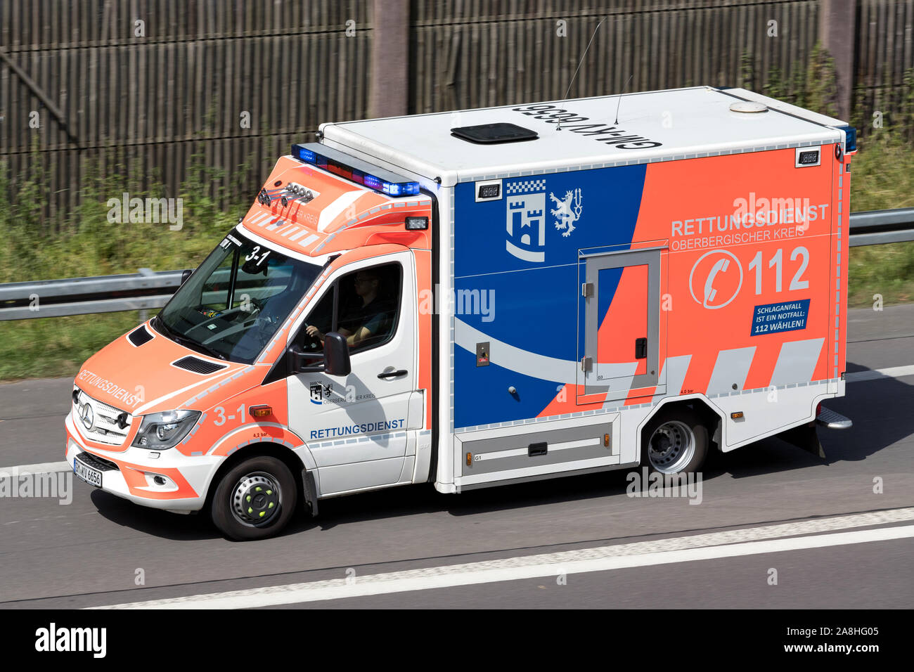 Ambulance of the German Oberberg distict with active blue emergency vehicle lighting on motorway. Stock Photo
