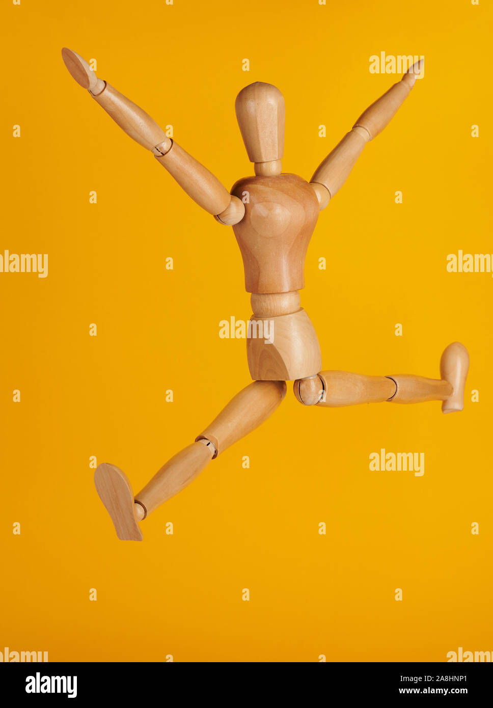 Wooden man in jumping pose isolated on yellow background Stock Photo