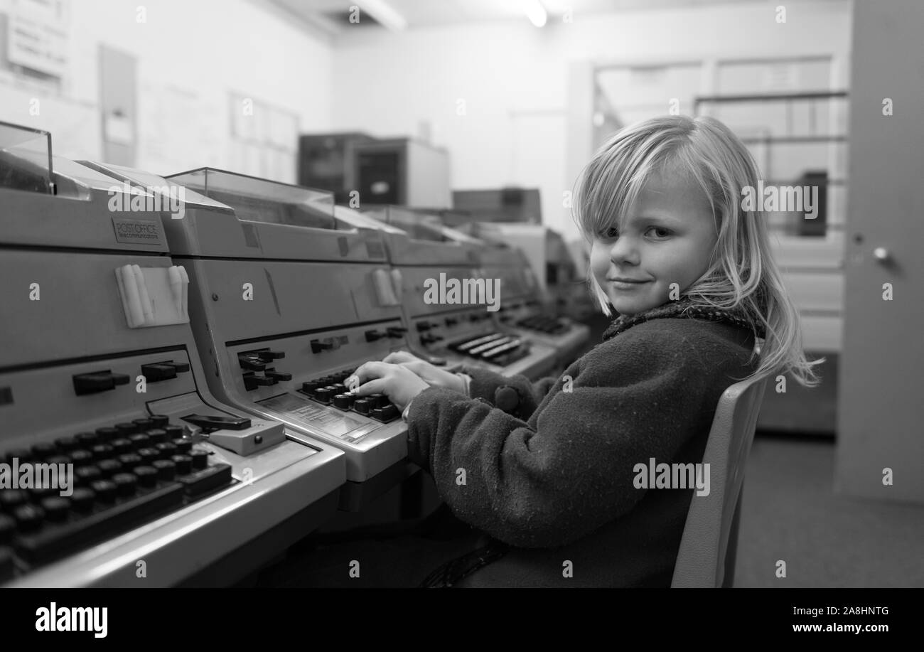 A cute little girl in a red coat sits at an old fashioned computer terminal at Kelvedon Hatch secret nuclear bunker museum, war preparations, Cold War Stock Photo