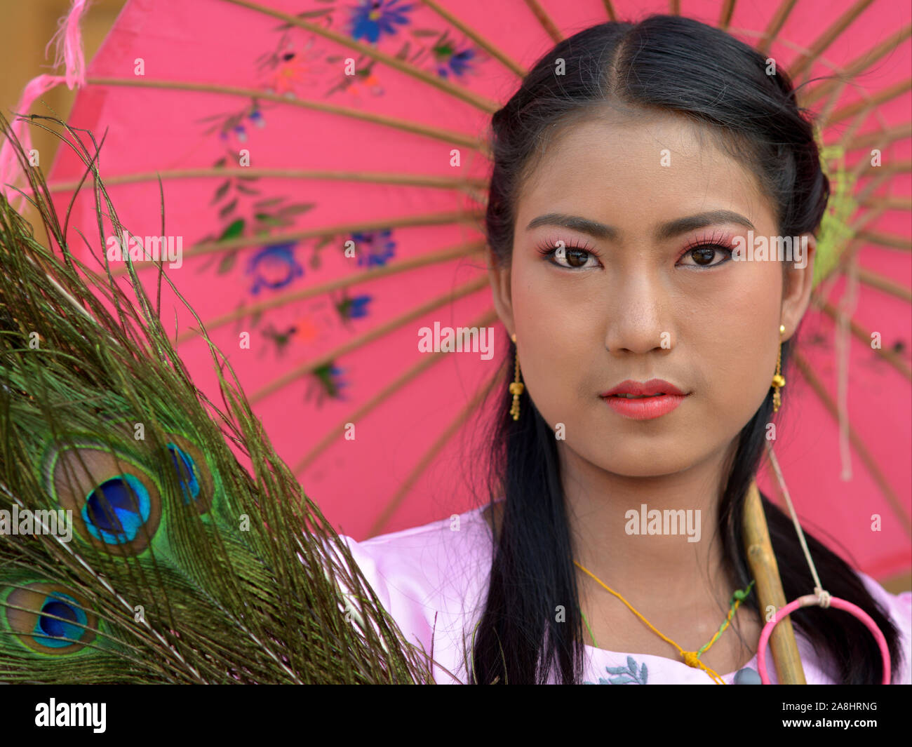 Burmese girl holds a colourful traditional paper parasol and poses for the camera during a traditional Buddhist celebration. Stock Photo