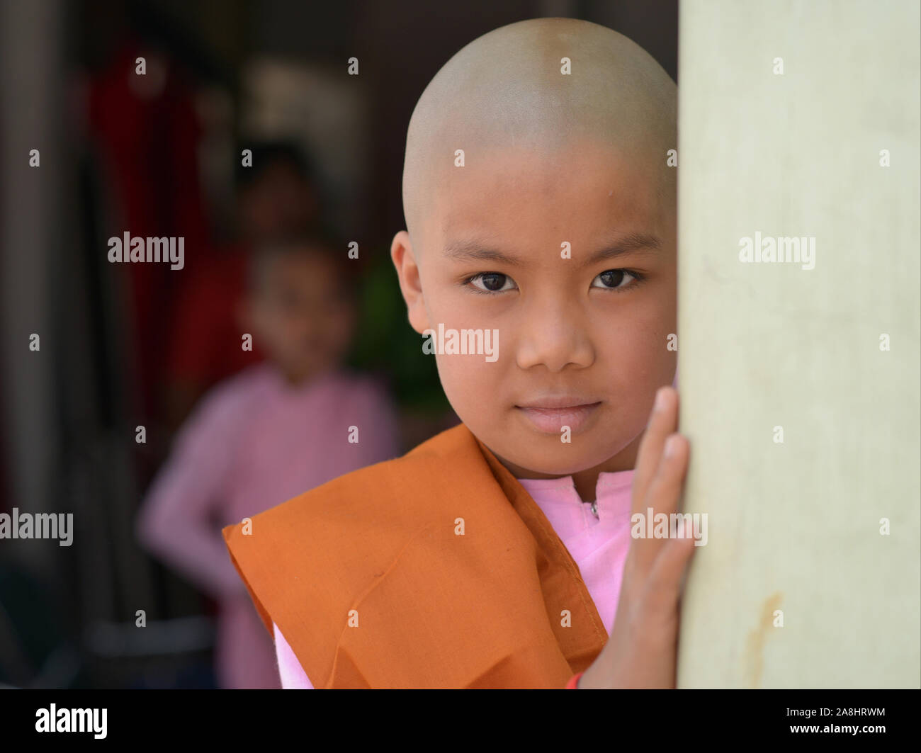 Cute little Burmese Buddhist girl nun (thilashin) with shorn head poses for the camera. Stock Photo