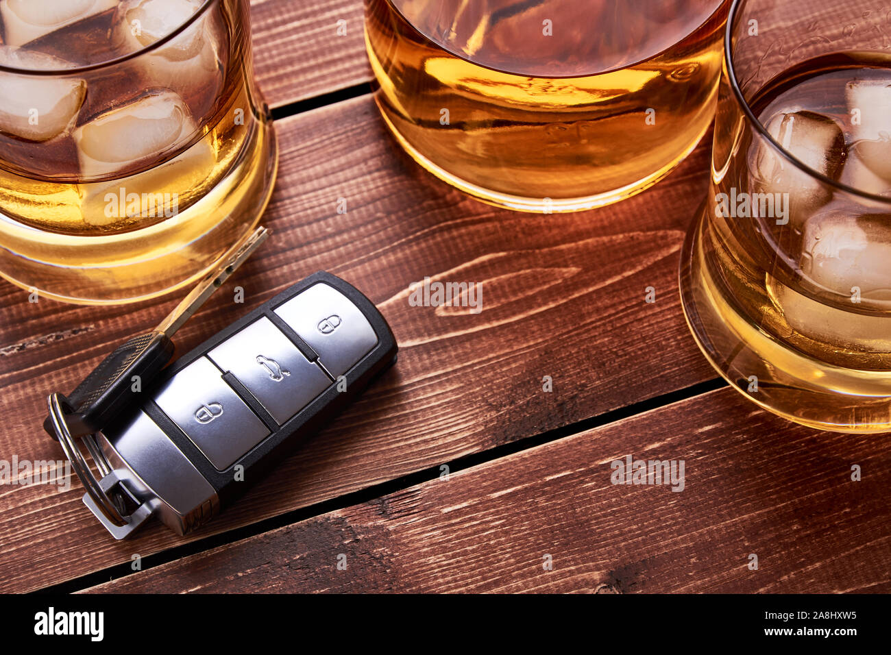 Modern car keys on wooden table top in bar. Glass and bottle of whiskey or other alcohol with ice. Suitable for the article on drunk driving. Stock Photo