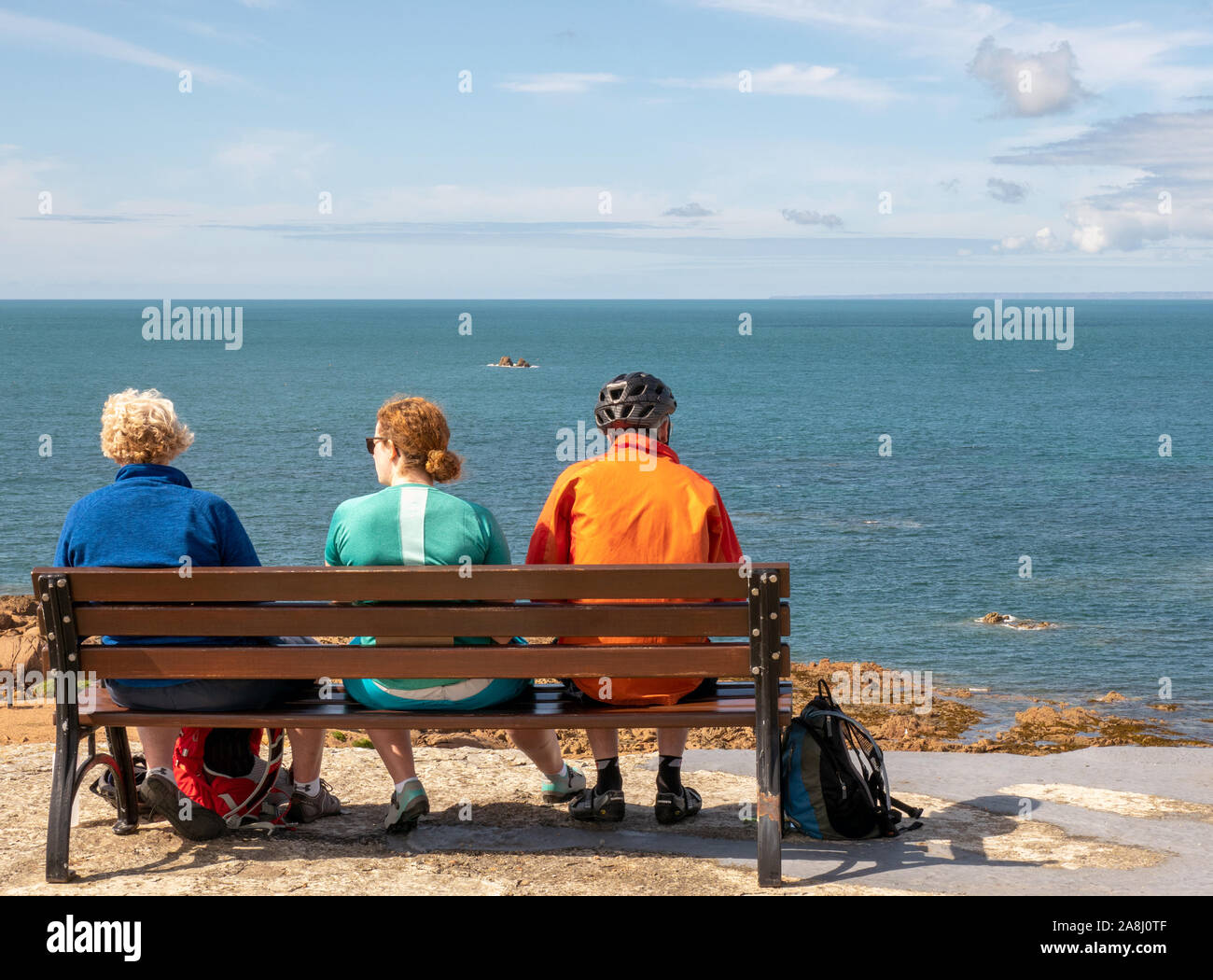 Three cyclists take a break at La Corbiere, Jersy, Channel Islands, UK. Stock Photo