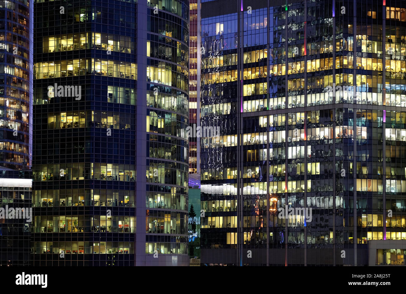 Glass walls of modern office buildings with many large panoramic windows in downtown business cluster with working people front view at night Stock Photo