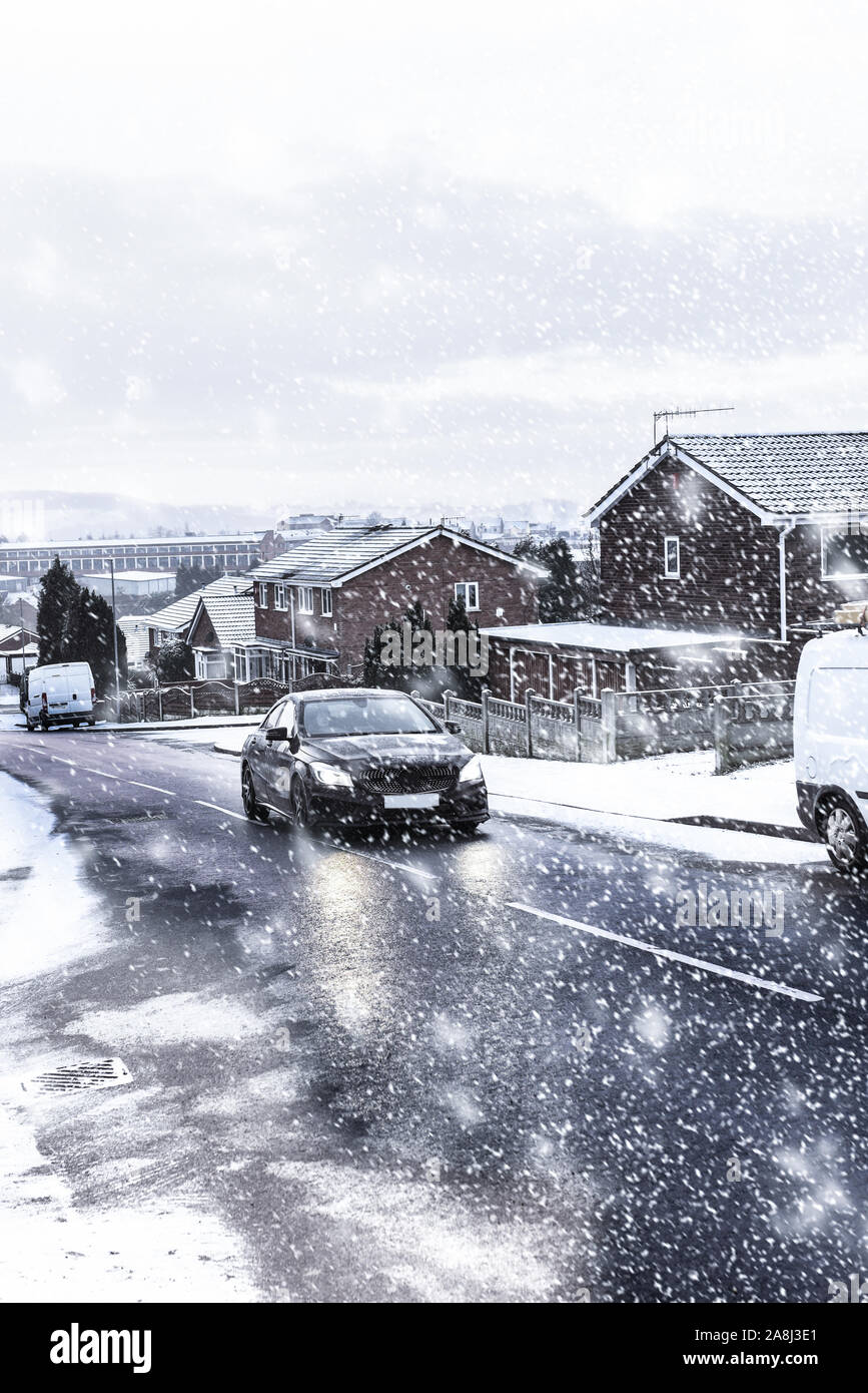Snow covered cars, recycling bins, roads and houses at night in Longton