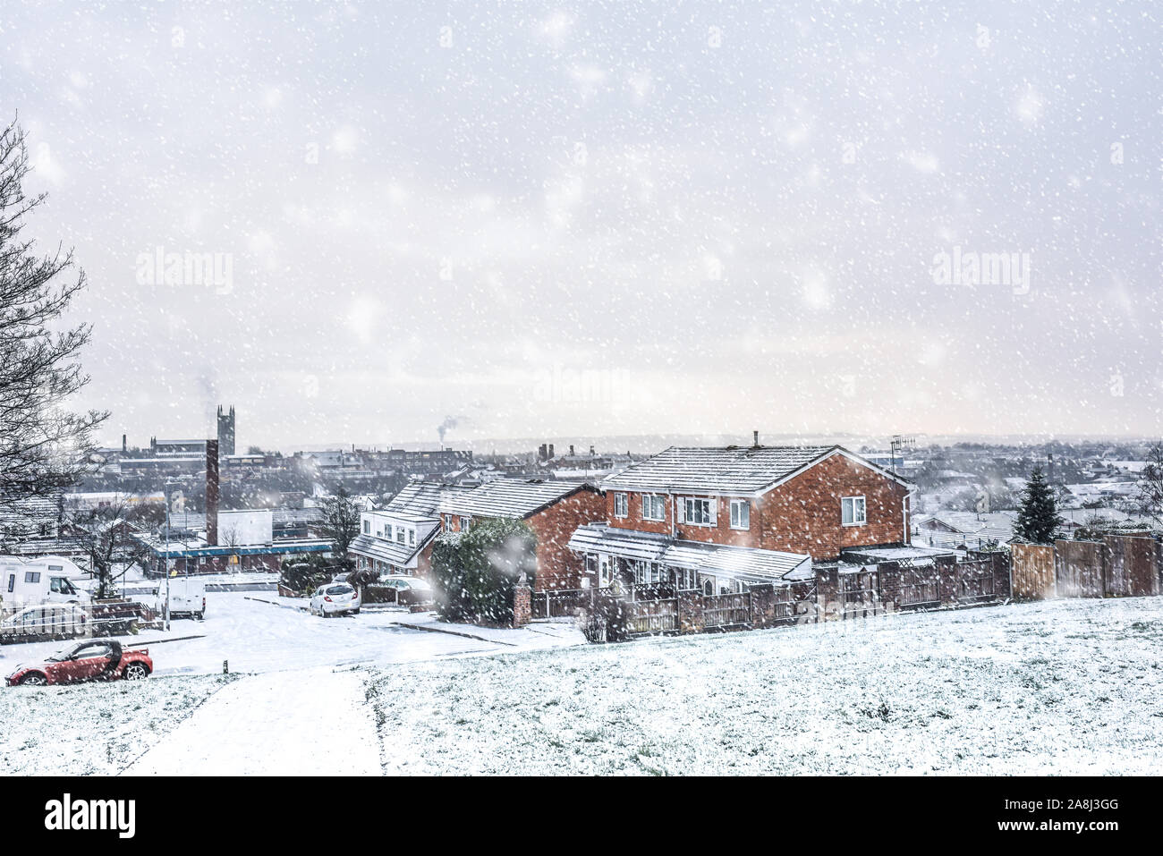 Snow covered cars, recycling bins, roads and houses at night in Longton