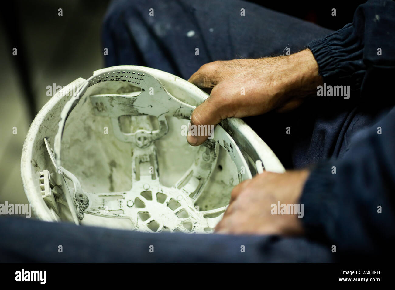 Details with the hands of a factory worker holding his dirty protective helmet. Stock Photo