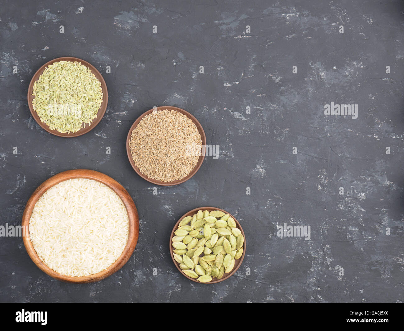 Rice, green cardamom, cumin, fennel on black concrete background with