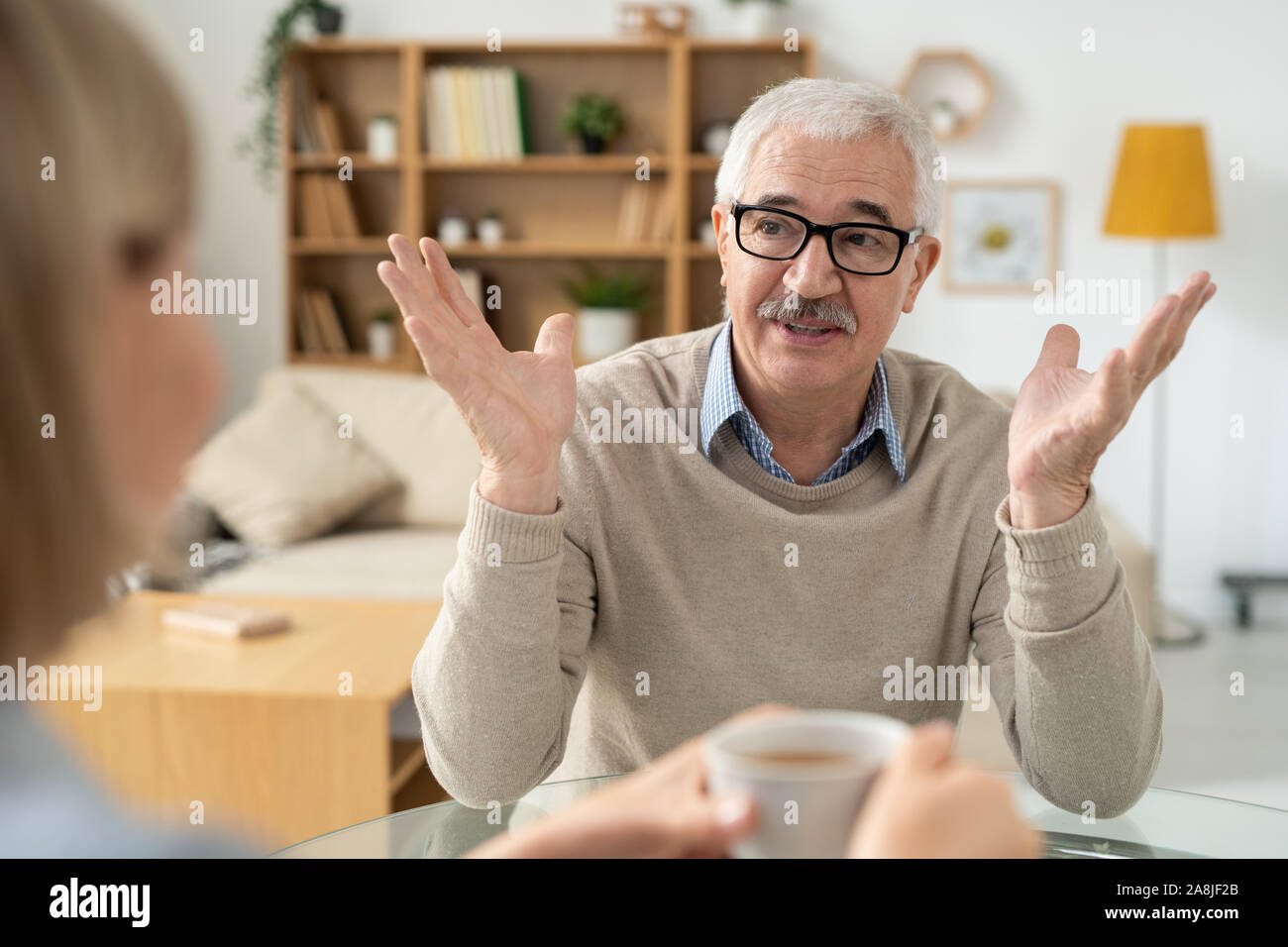 Aged man explaining something to his daughter while both having tea at home Stock Photo