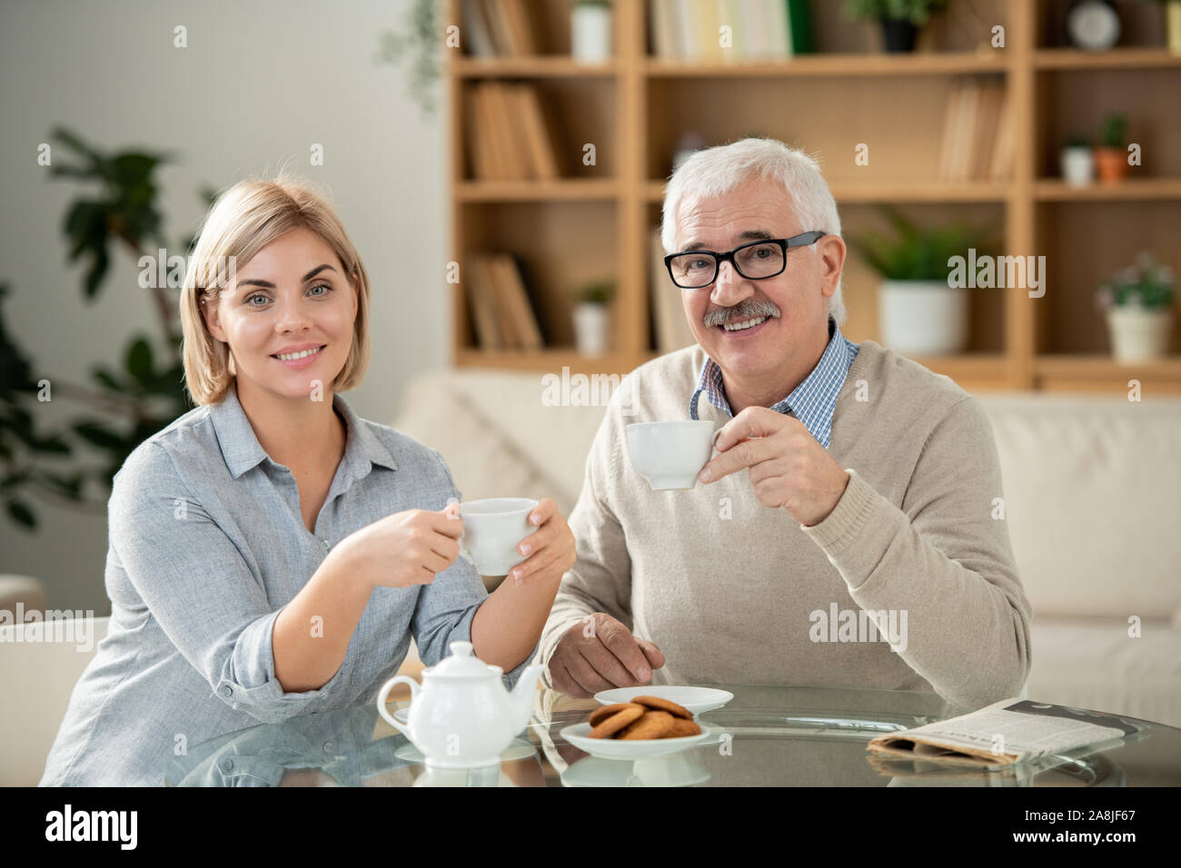 Smiling young woman and her senior father having tea by served table at home Stock Photo