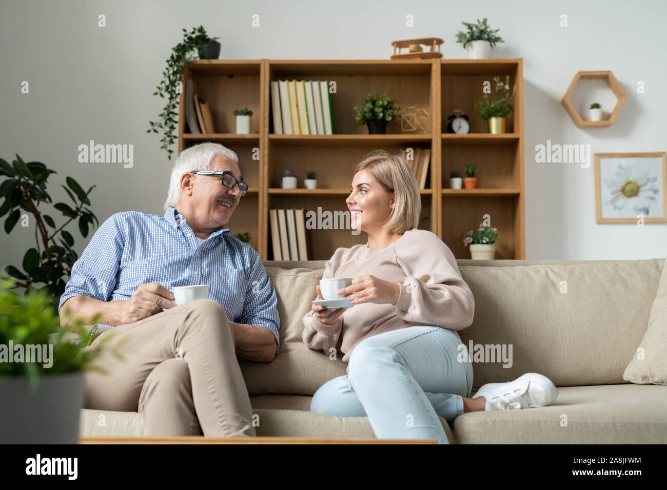 Young female and her father having tea while relaxing and chatting on couch Stock Photo