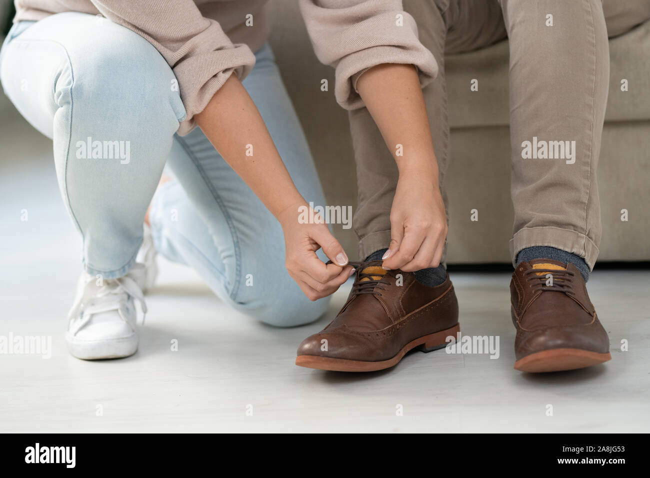 Young woman in casualwear helping her disable father to tie shoelaces