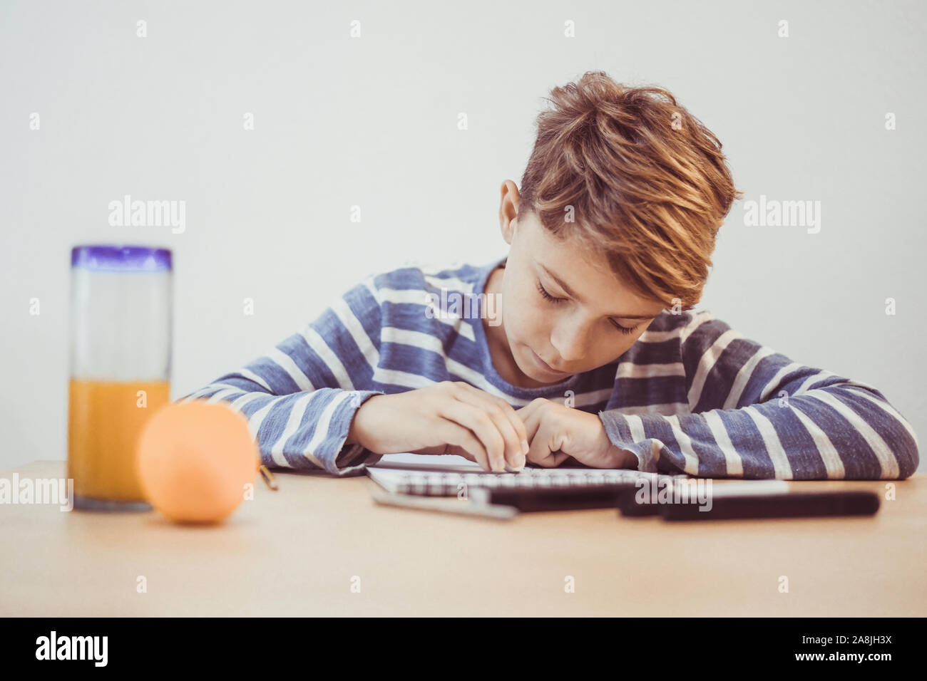 Student drawing with pencil on the notebook. Boy doing homework writing on a paper. Kid hold a pencil and draw a manga at home. Teen drawing sitting a Stock Photo