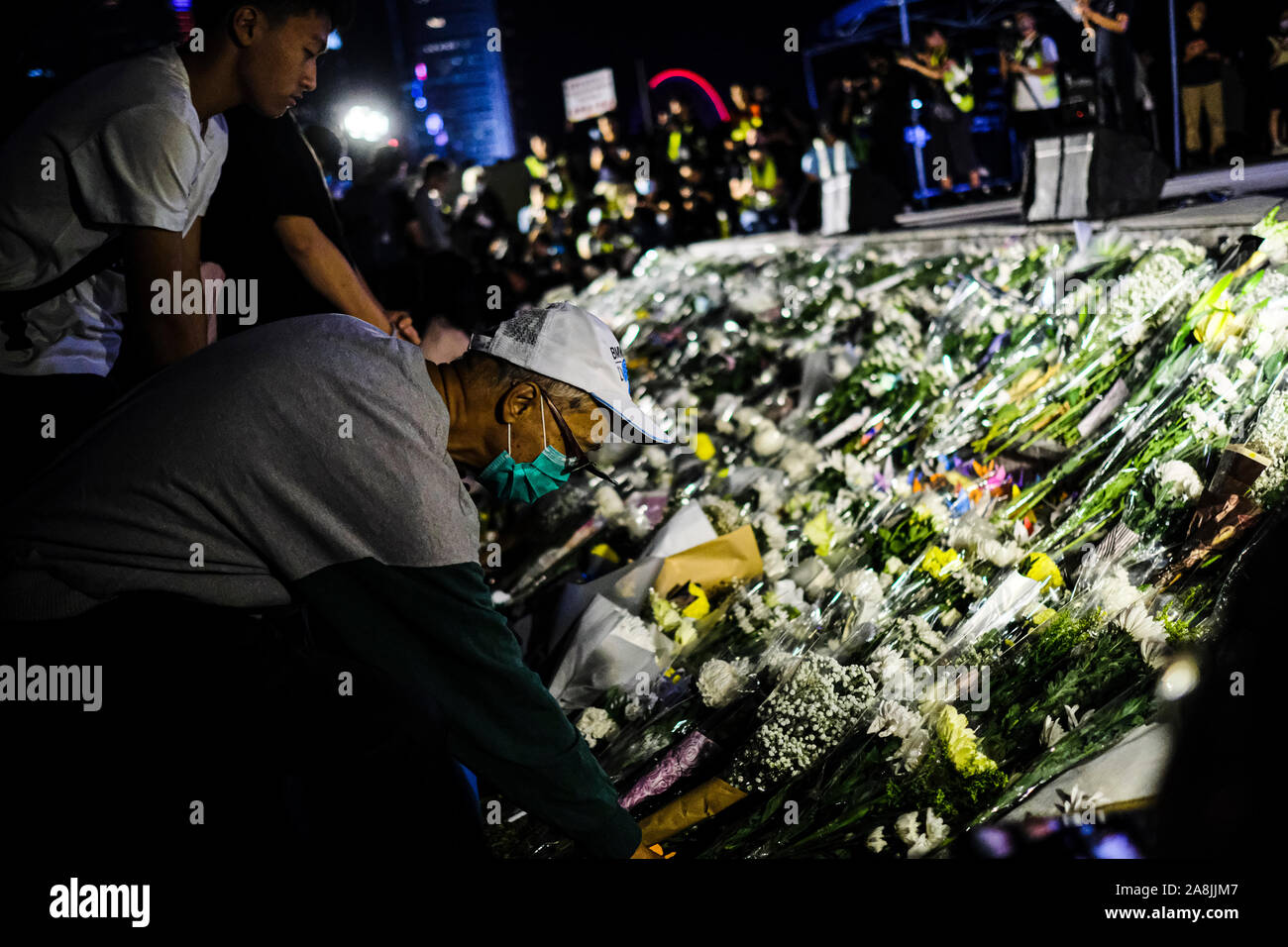 Demonstrators placing flowers at the memorial during the rally.Memorial rally at Tamar Park in Hong Kong to mourn the death of a 22 years old university student, Alex Chow Tsz Lok who died from a serious brain injury during a fall on November 4th as police skirmished with demonstrators last weekend. He was left in critical condition and died after suffering a cardiac arrest. Stock Photo