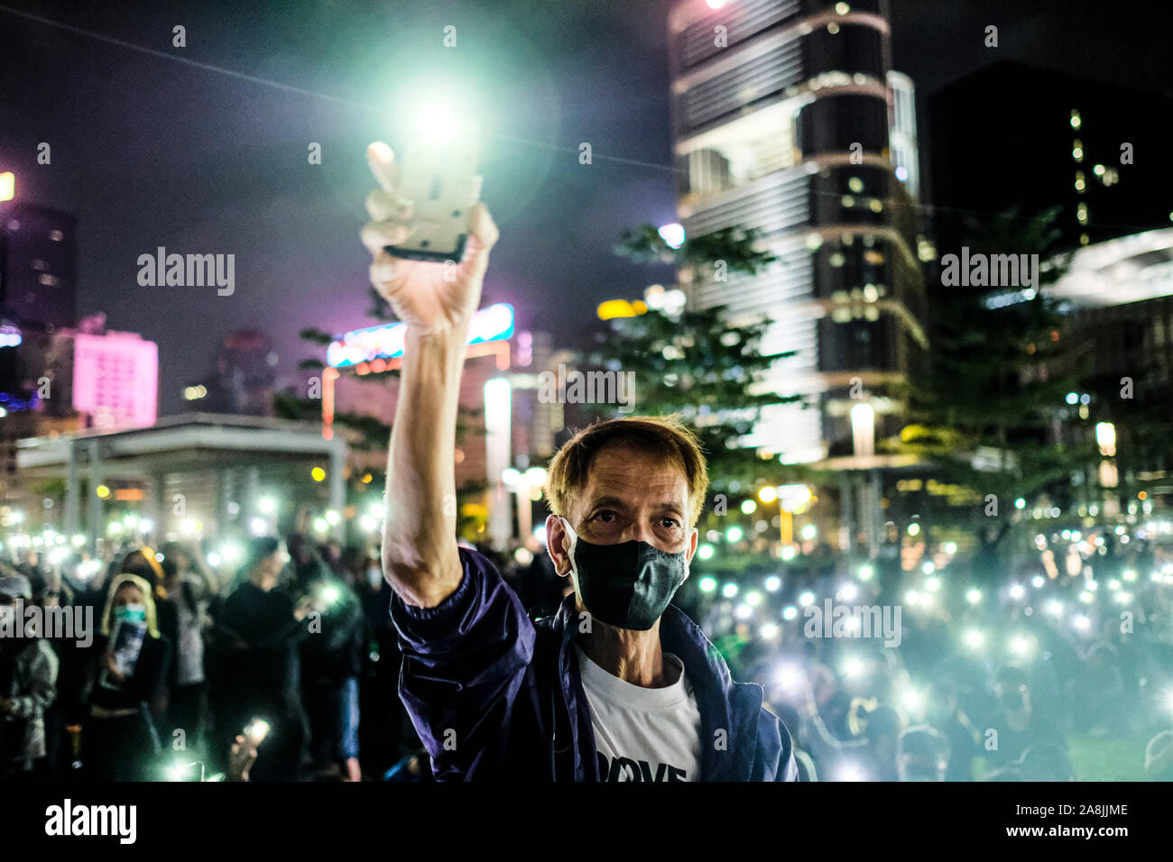 A man holds up his smartphone light during the rally.Memorial rally at Tamar Park in Hong Kong to mourn the death of a 22 years old university student, Alex Chow Tsz Lok who died from a serious brain injury during a fall on November 4th as police skirmished with demonstrators last weekend. He was left in critical condition and died after suffering a cardiac arrest. Stock Photo