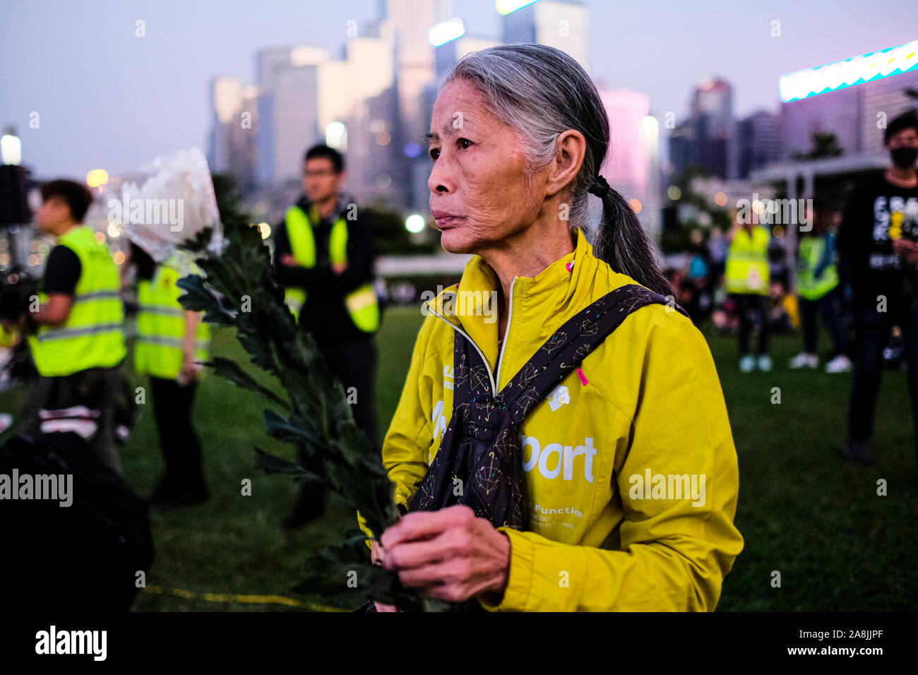 A senior woman with flowers during the rally.Memorial rally at Tamar Park in Hong Kong to mourn the death of a 22 years old university student, Alex Chow Tsz Lok who died from a serious brain injury during a fall on November 4th as police skirmished with demonstrators last weekend. He was left in critical condition and died after suffering a cardiac arrest. Stock Photo