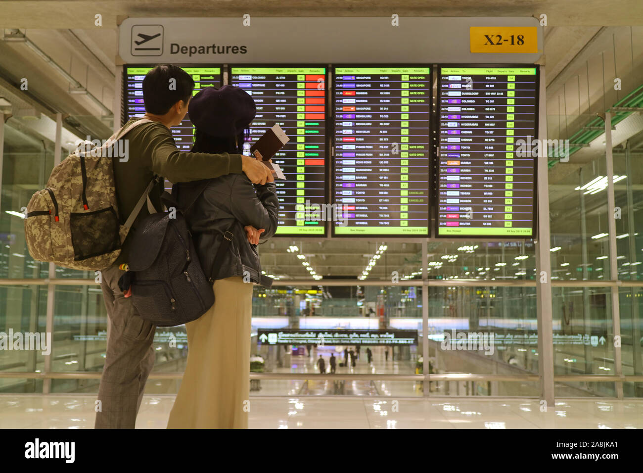 Young couple with passport in hands looking at blurry flight information screen at the airport Stock Photo