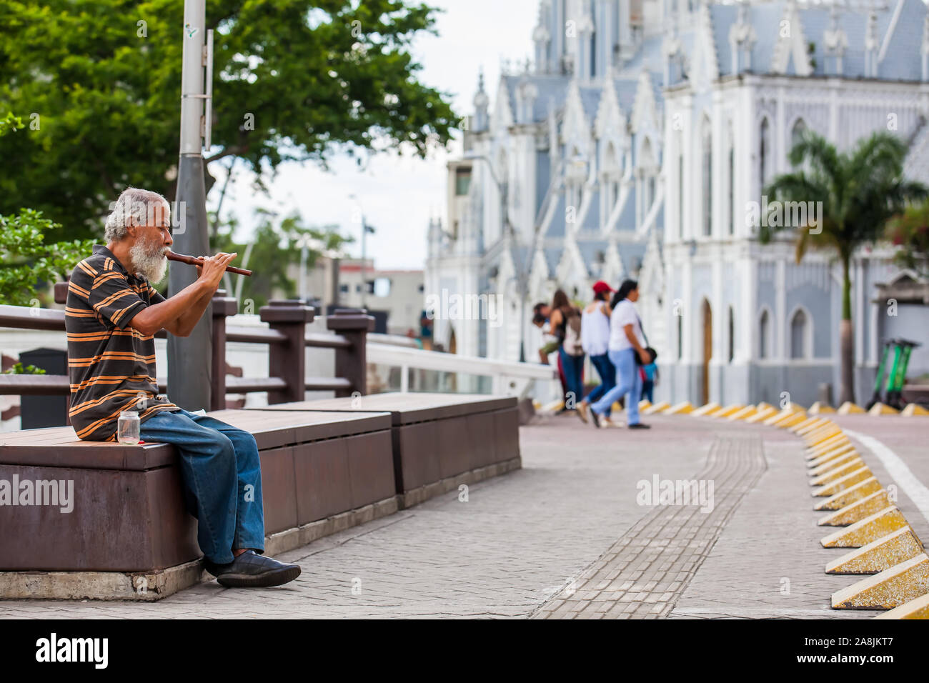 CALI, COLOMBIA - OCTOBER, 2019: Old man playing his flute to get money at the River Boulevard in Cali Stock Photo