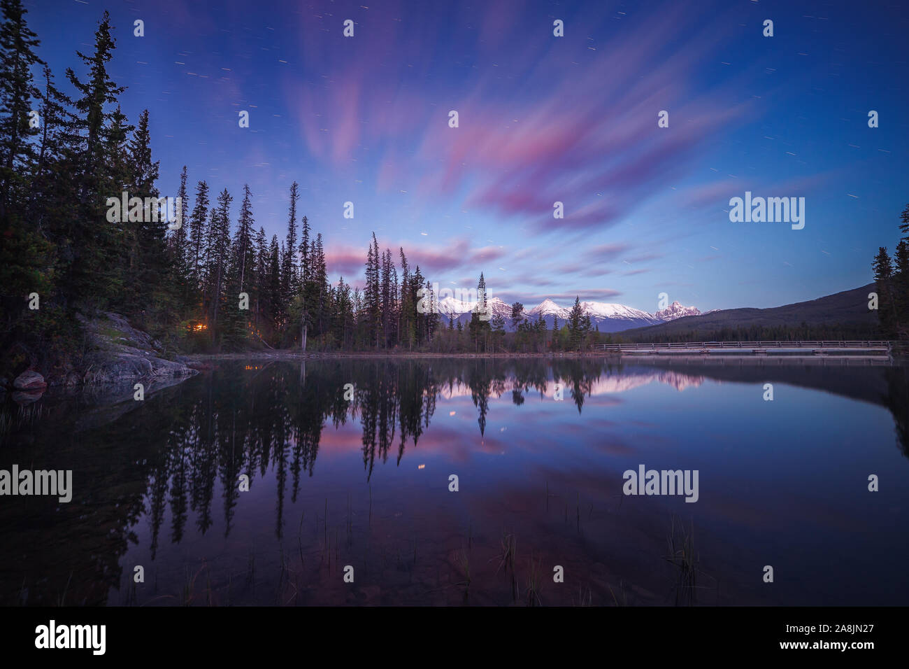 Before sunrise at Pyramid Lake. Mirror like waters, reflected mountains, trees and clouds. Blue hour and calm morning. Jasper National Park, Canada. Stock Photo