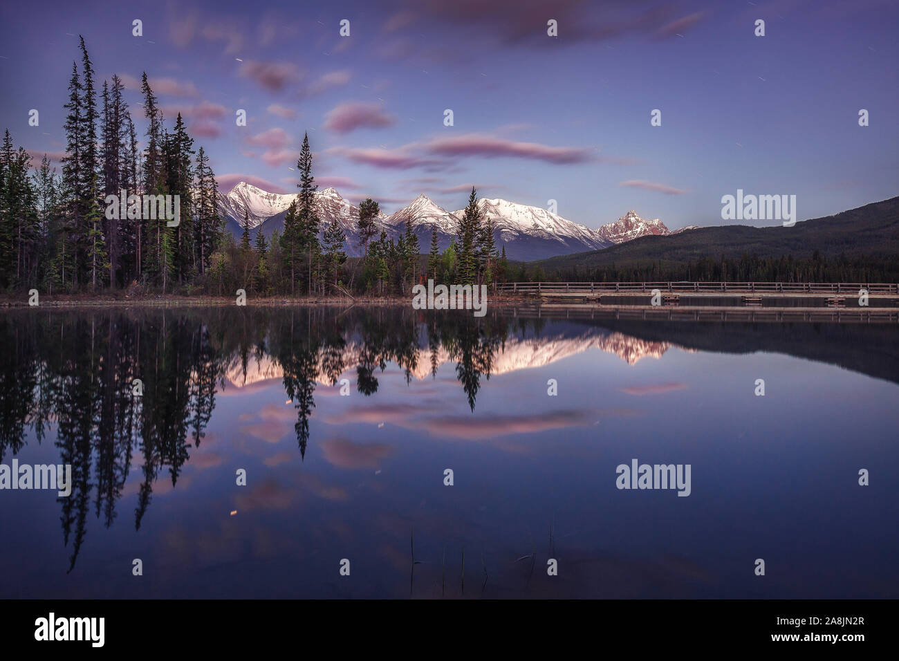 Before sunrise at Pyramid Lake. Mirror like waters, reflected mountains, trees and clouds. Blue hour and calm morning. Jasper National Park, Canada. Stock Photo
