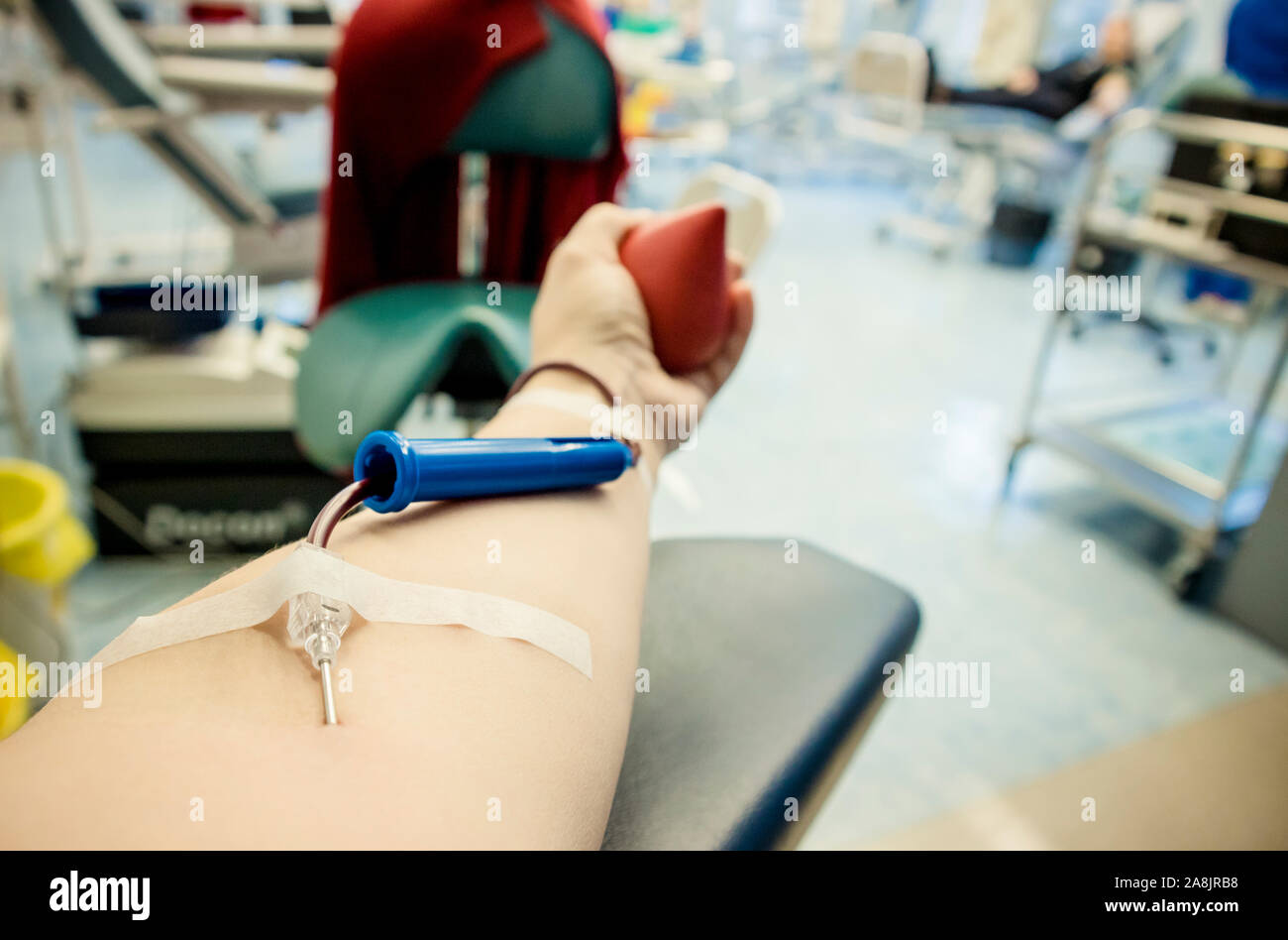Selective focus on woman arm hand with needle inside skin, blood flowing through blood donation equipment. Happy positive woman donor donating blood c Stock Photo