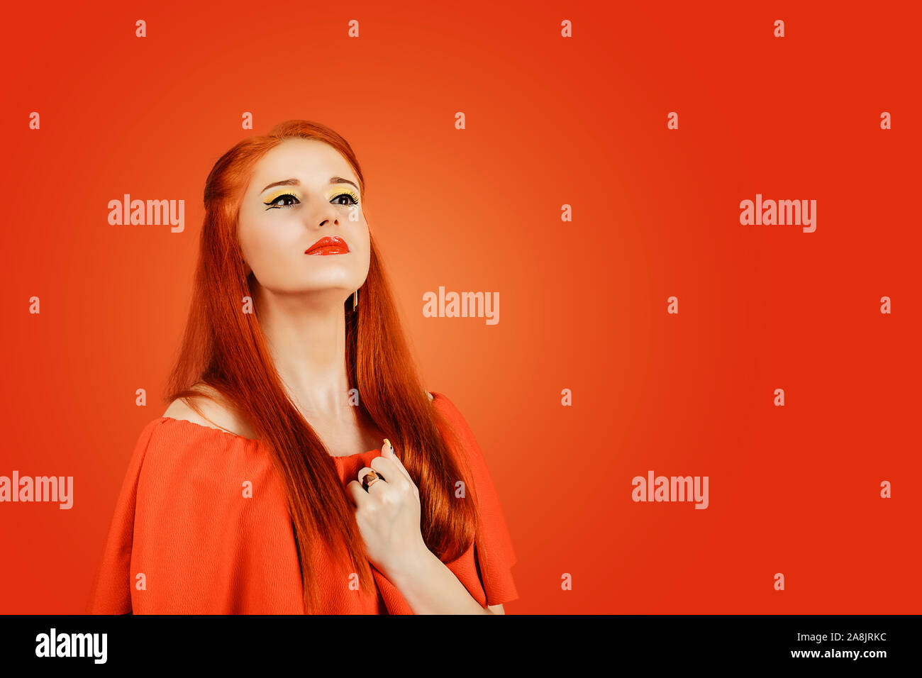 Self-esteem. Redhead woman in red dress holding hand to her chest, being proud of herself, feeling self-important, having napoleon syndrome concept is Stock Photo