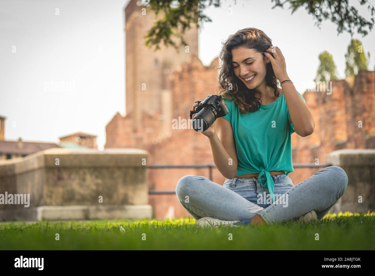 Photographer girl sitting on the grass looking at the camera screen, smiling Stock Photo