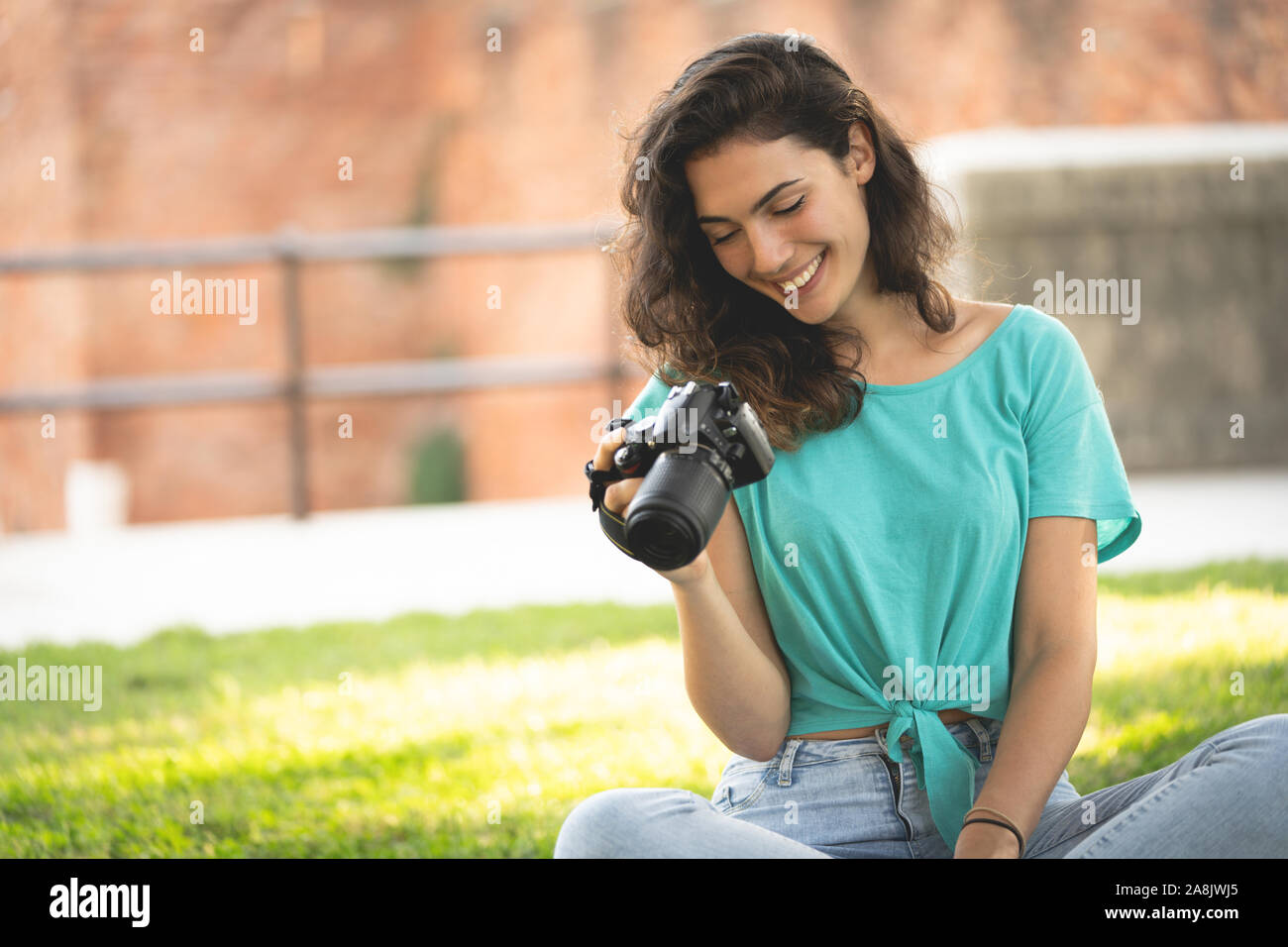 Photographer girl sitting on the grass looking at the camera screen, smiling Stock Photo