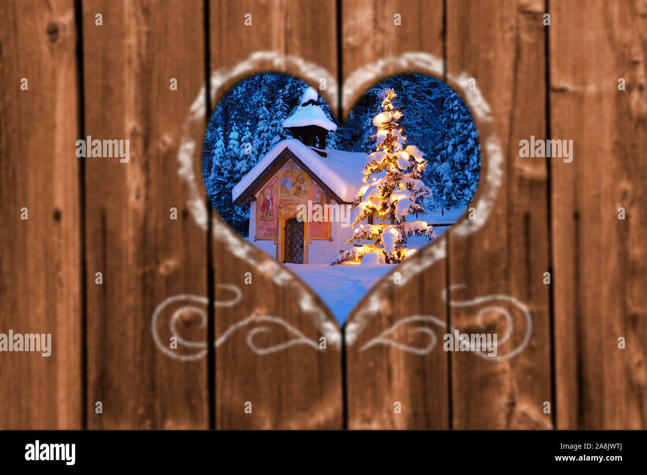 Looking through a carved heart in a wooden wall to a romantic and illuminated Christmas chapel Stock Photo