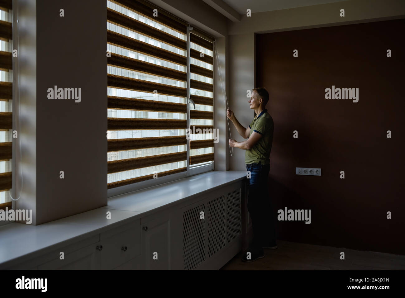 The man is pulling the chain to open the roller blinds. Stock Photo