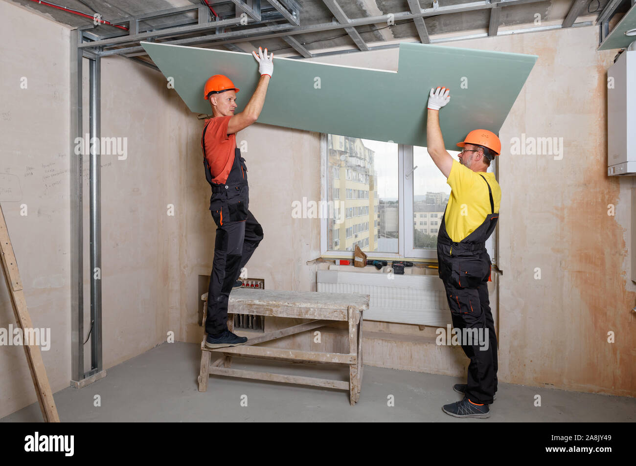 Workers are lifting plasterboard for further attaching to the ceiling. Stock Photo