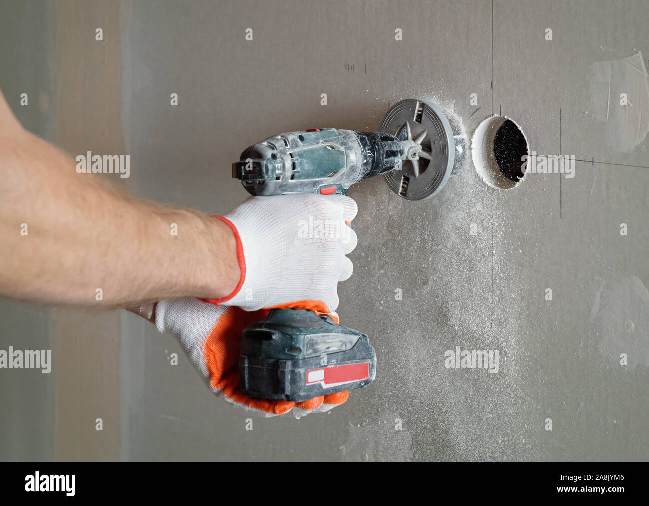 A worker is making holes in the drywall to install the outlet in the