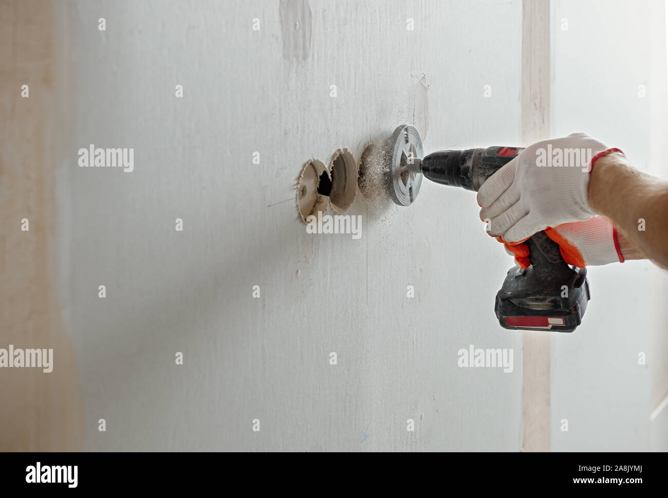 A worker is making holes in the drywall to install the outlet in the