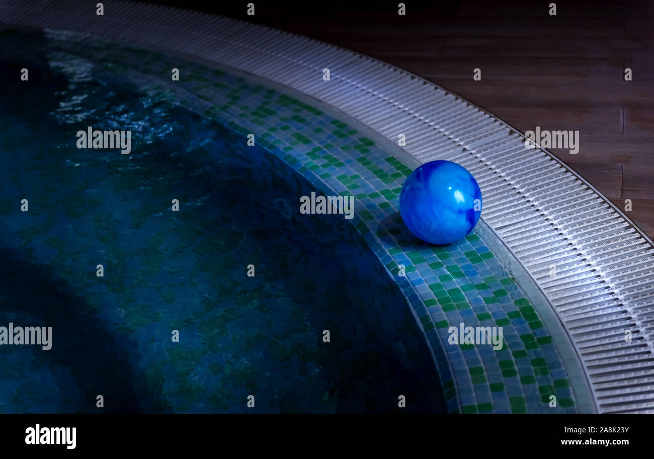 Blue ball is left on side of swimming pool decorated with mosaic tiles. Stairs are visible through shallow water. Summer season and private safety on Stock Photo