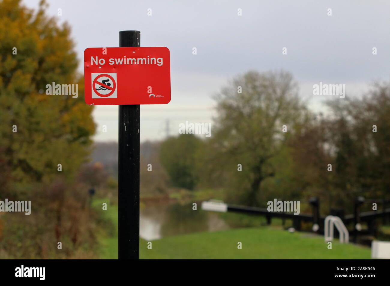 Red No Swimming sign mounted on a black pole by a canal lock Stock Photo