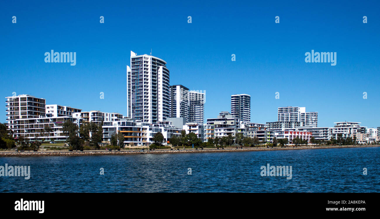 Large waterfront houses, apartment condominiums in suburban community on harbour with tree lined walkway, blue sky in background Stock Photo