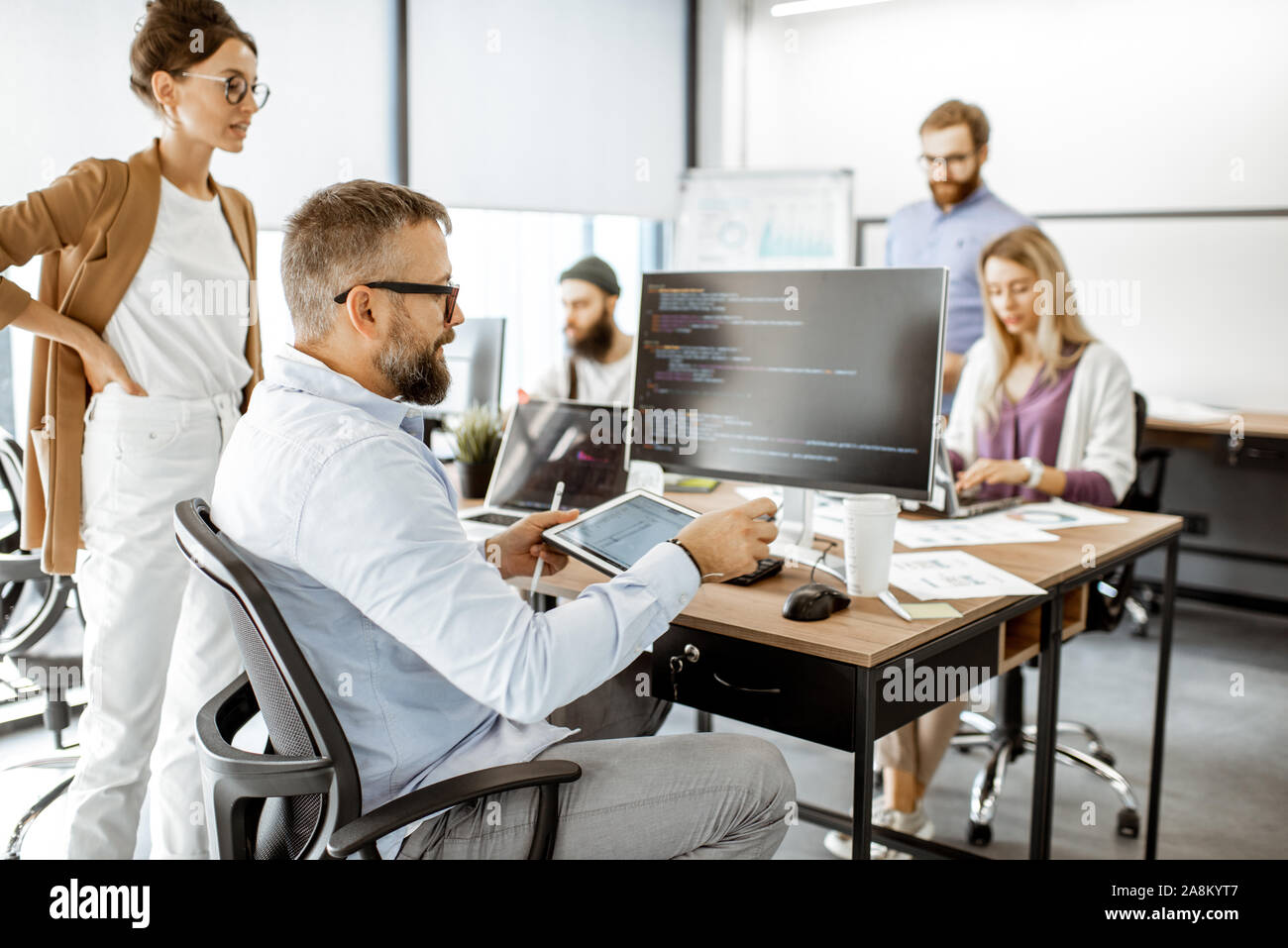 Group of diverse colleagues working on the computers in the modern office or coworking space, writing programming code Stock Photo