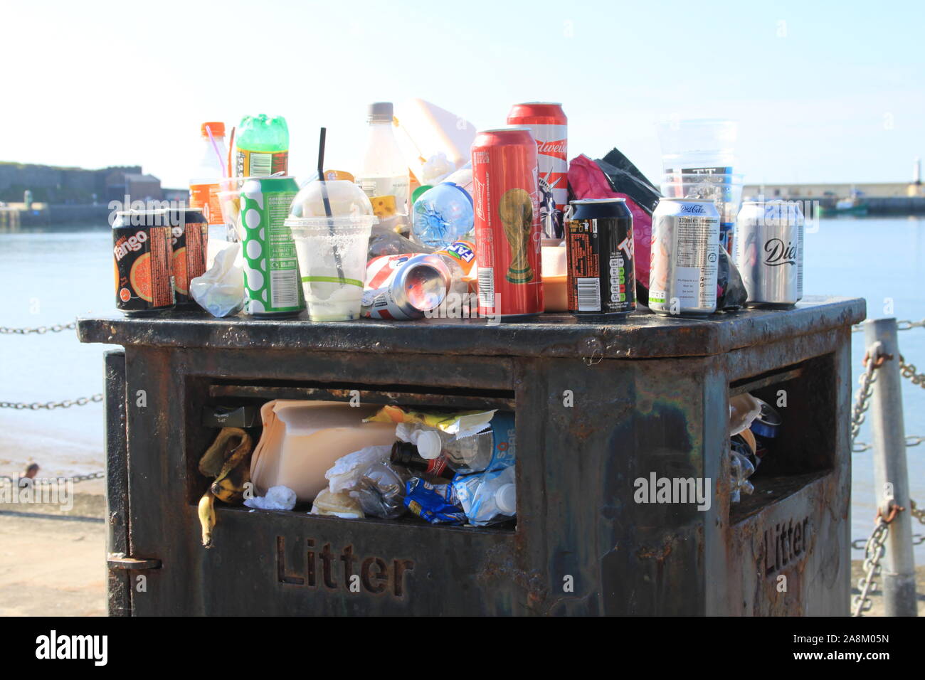 Overflowing rubbish bin / trash can / litter bin at the seaside with empty cans, plastic bottles