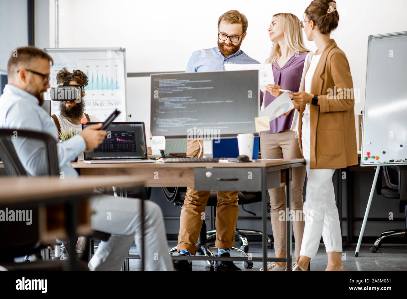 Group of diverse colleagues working with computers in the modern office or coworking space, writing programming code and working with vr goggles Stock Photo